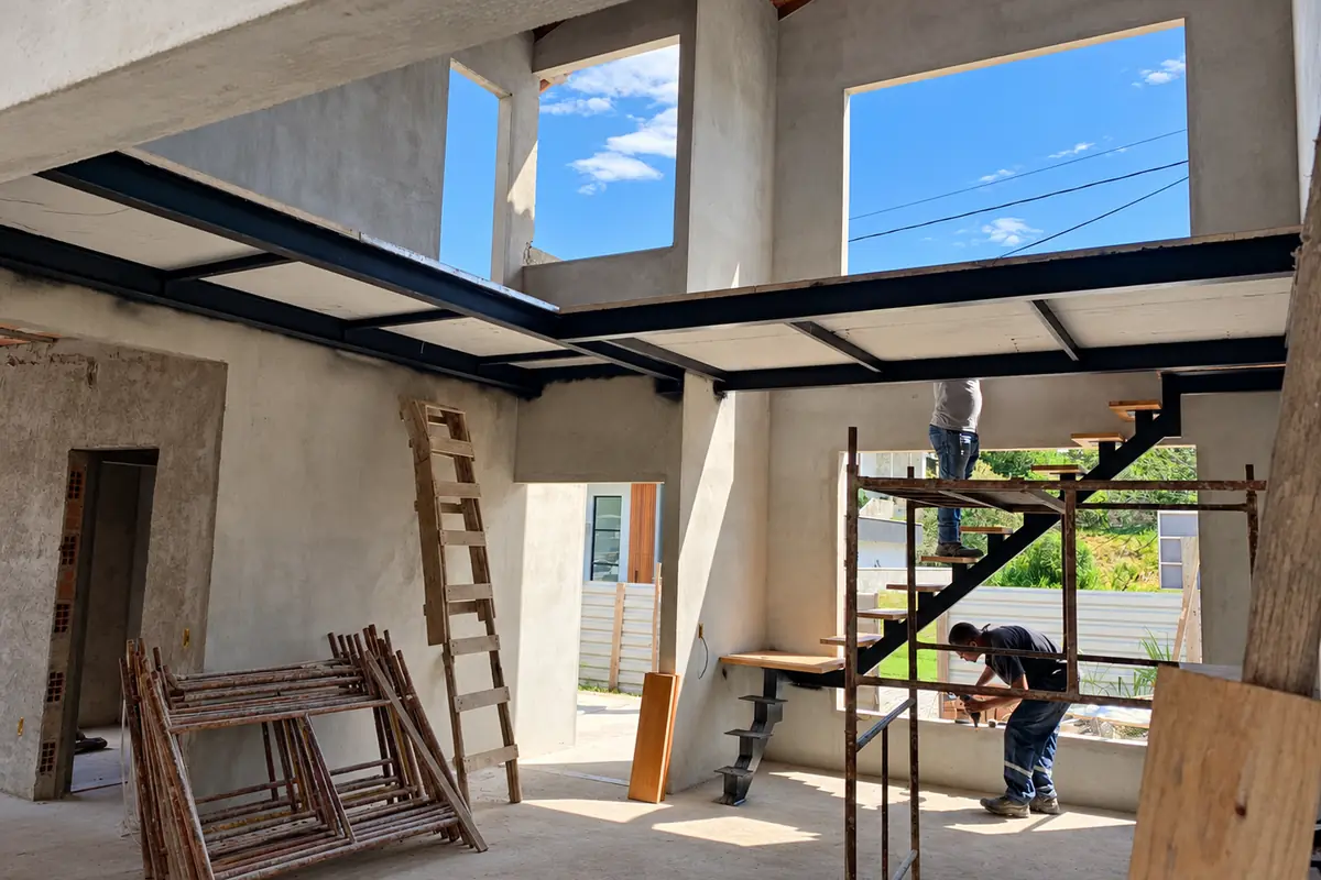 Estrutura metálica da escada sendo montada na obra, com um instalador no andaime