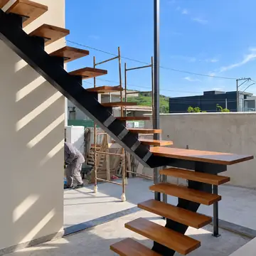 Escada externa de viga central preta com degraus de madeira, ao ar livre, com um instalador ao fundo