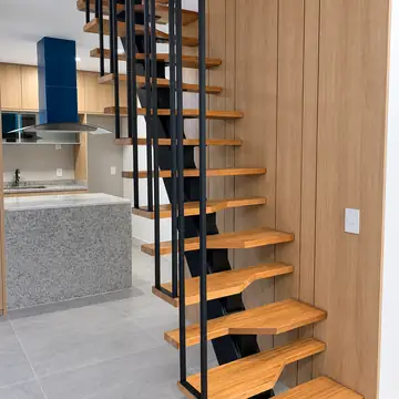 Escada de viga central com degraus de madeira recortados e guarda-corpo de barras, ao lado da cozinha